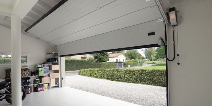 Open garage door with storage shelves inside, revealing a driveway and a house in the background.