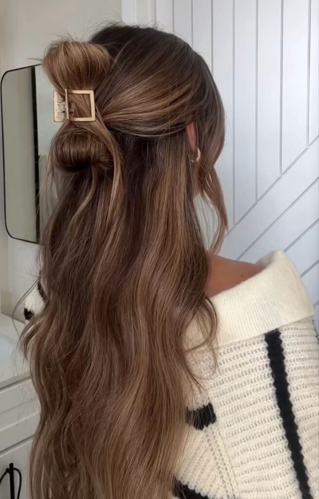 Woman with long, wavy hair styled in a half-up bun with a stylish gold hair clip, wearing a cozy sweater.