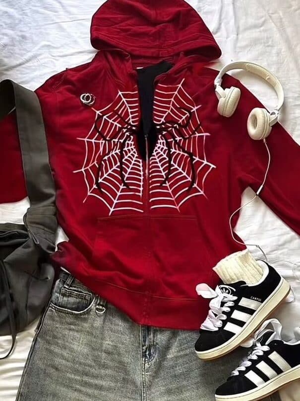 Red hoodie with spider design, denim shorts, black sneakers, white headphones, and backpack laid on white background.