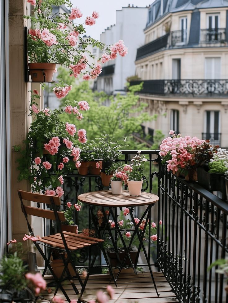 Charming balcony with pink flowers, wrought iron railing, and a small bistro table, overlooking a Parisian street scene.