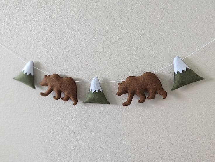 Felt garland with brown bears and green snowy mountains, hanging on a white wall.