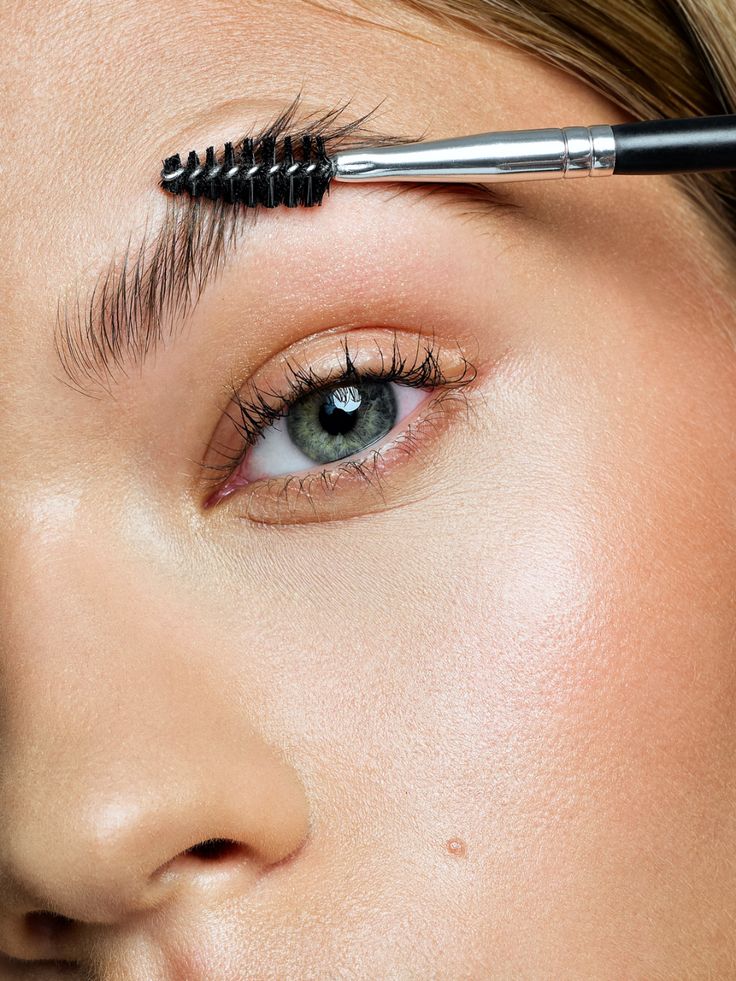 Close-up of an eyebrow being brushed with a spoolie, showcasing groomed and defined eyebrows for beauty care.