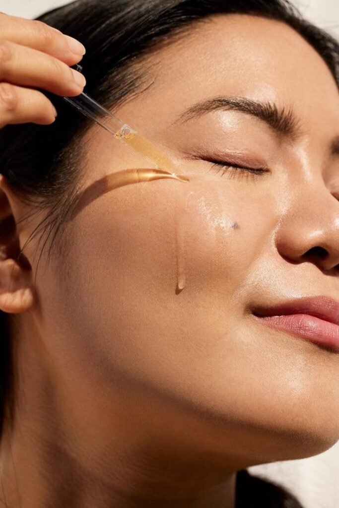 Woman applying facial serum with a dropper for skincare routine and glowing skin.