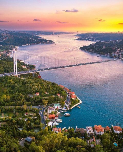 Aerial view of scenic sunset over Bosphorus Strait and bridge, Istanbul; lush greenery and vibrant cityscape.
