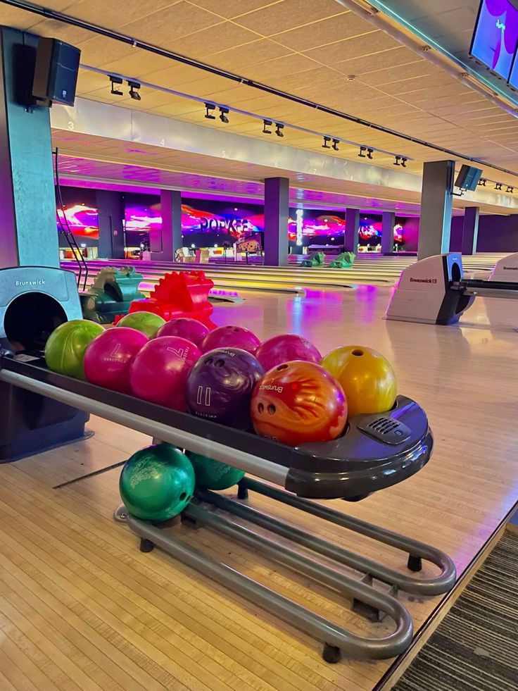Bowling 🎳 Colorful bowling balls on a rack at a vibrant bowling alley with lit lanes in the background. | Sky Rye Design Colorful bowling balls on a rack at a vibrant bowling alley with lit lanes in the background.