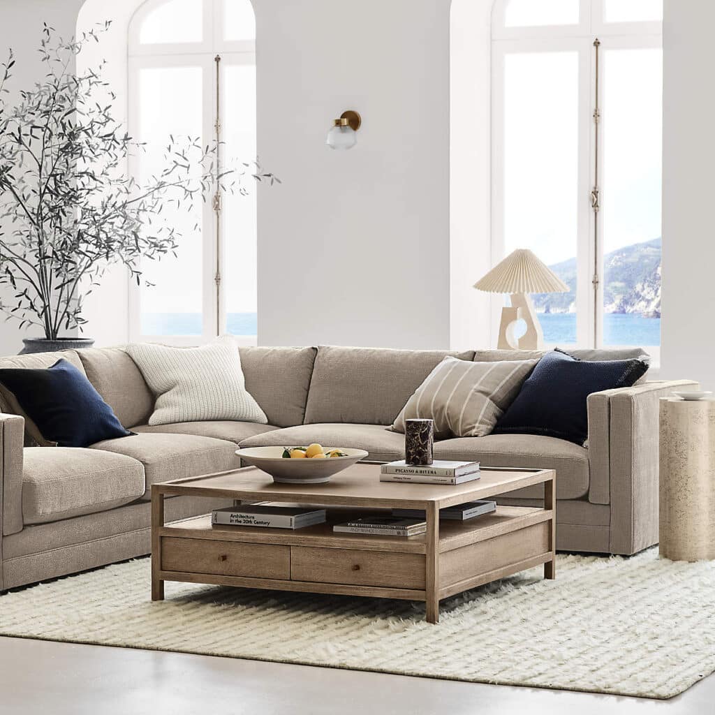Cozy living room with beige sectional sofa, wooden coffee table, and ocean view through large windows.