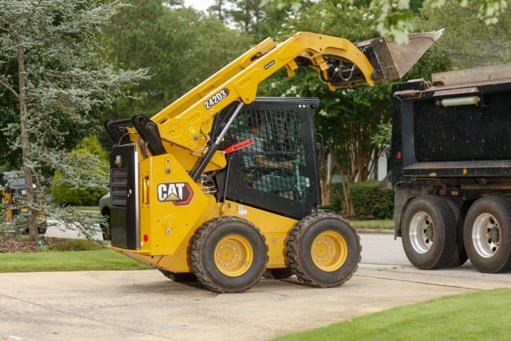 CM20190826-03000-4024f Yellow skid steer loader lifting soil into dump truck on a construction site. | Sky Rye Design Yellow skid steer loader lifting soil into dump truck on a construction site.