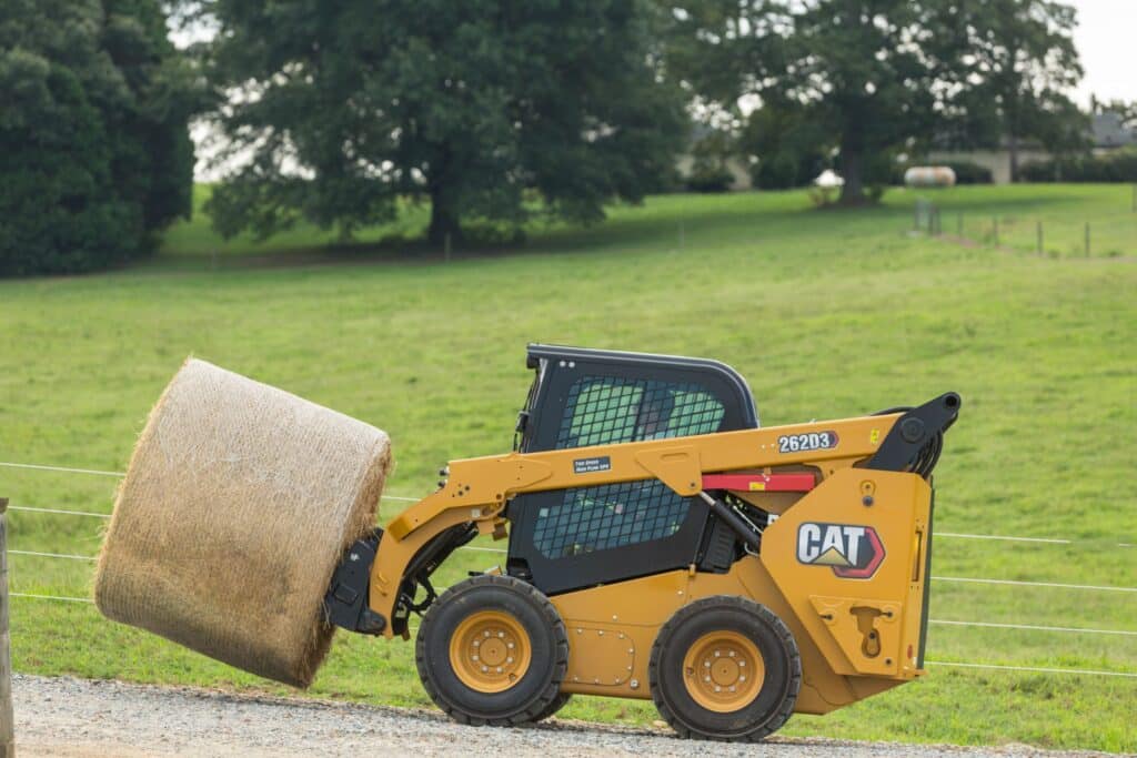 Yellow loader moving hay bale on green farm field.