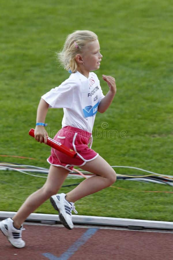 Young girl running in a relay race on a track, holding a baton, focused and determined.