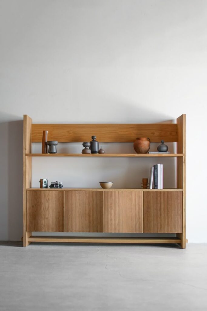 Minimalist wooden cabinet with shelves, decorated with books and pottery against a plain white background.