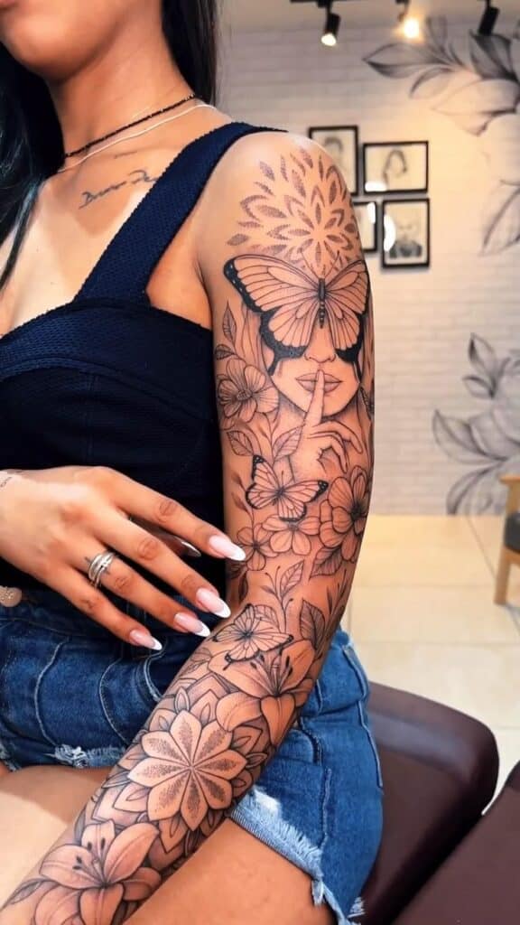Detailed floral and butterfly tattoo on woman's arm, showcasing intricate design and artistry in a tattoo studio.