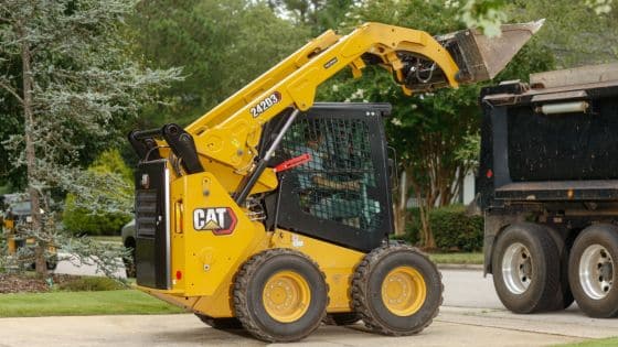 Choosing Skid Steer Loader Benefits of New Machine Yellow skid steer loader lifting materials into a truck, outdoors with trees in the background. | Sky Rye Design Yellow skid steer loader lifting materials into a truck, outdoors with trees in the background.