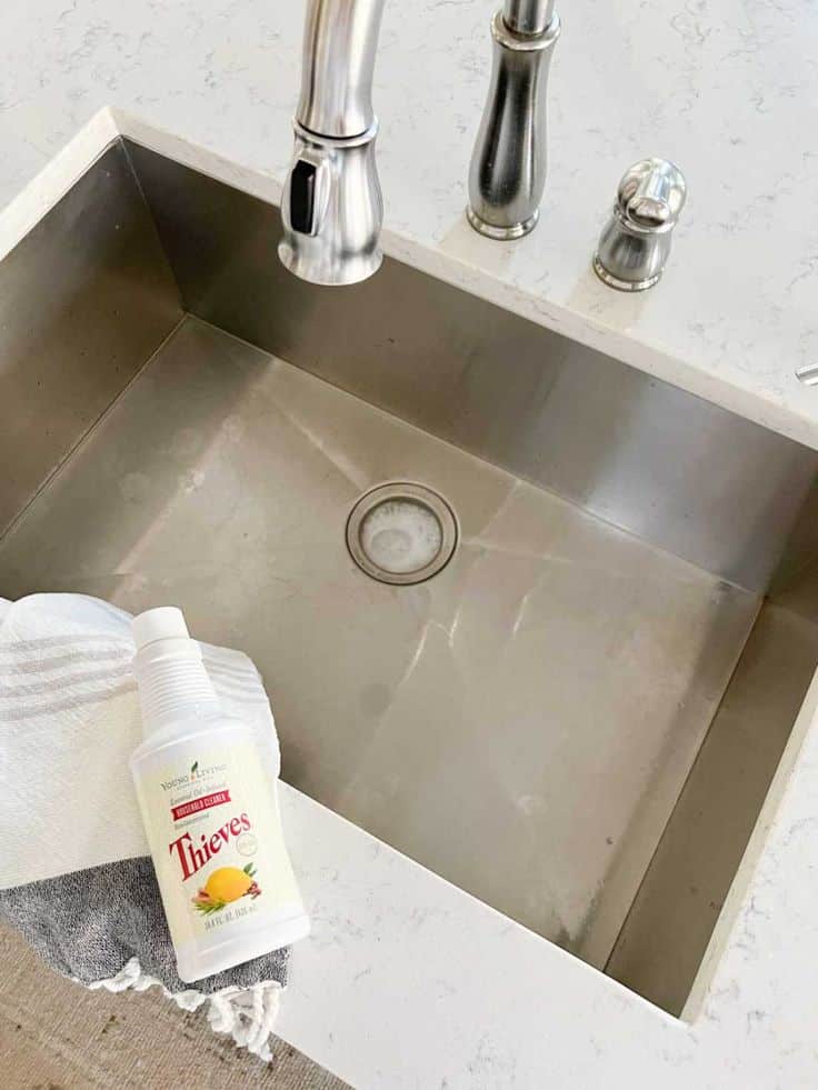 Bottle of Thieves cleaner on countertop next to stainless steel sink with faucet in a kitchen setting.