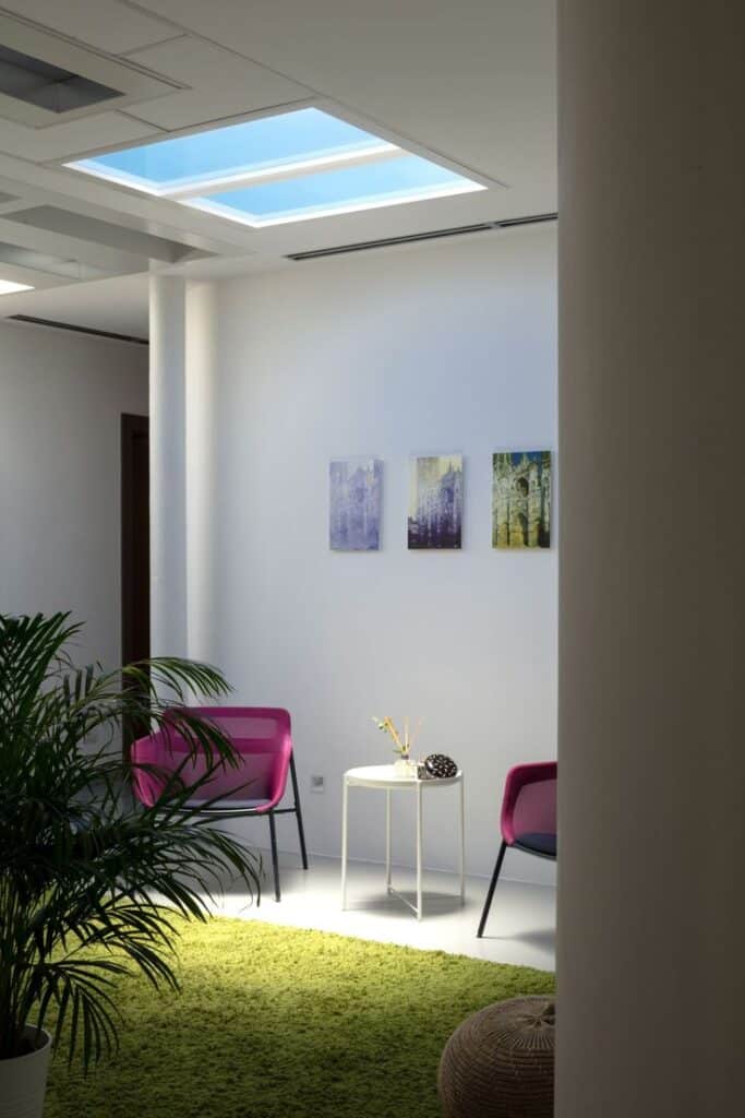 Modern lounge with skylight, pink chairs, green rug, and wall art, creating a bright and inviting atmosphere.