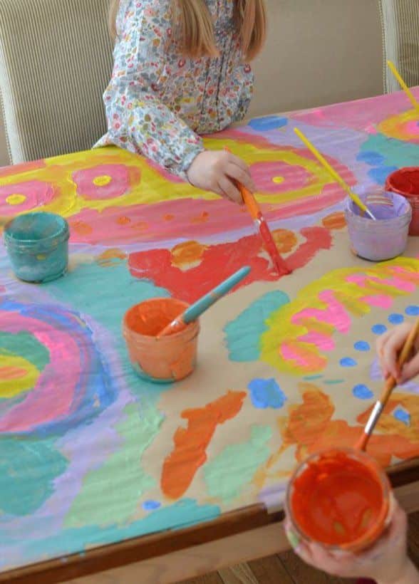 Children painting a colorful abstract mural on a table with vibrant paints and brushes.