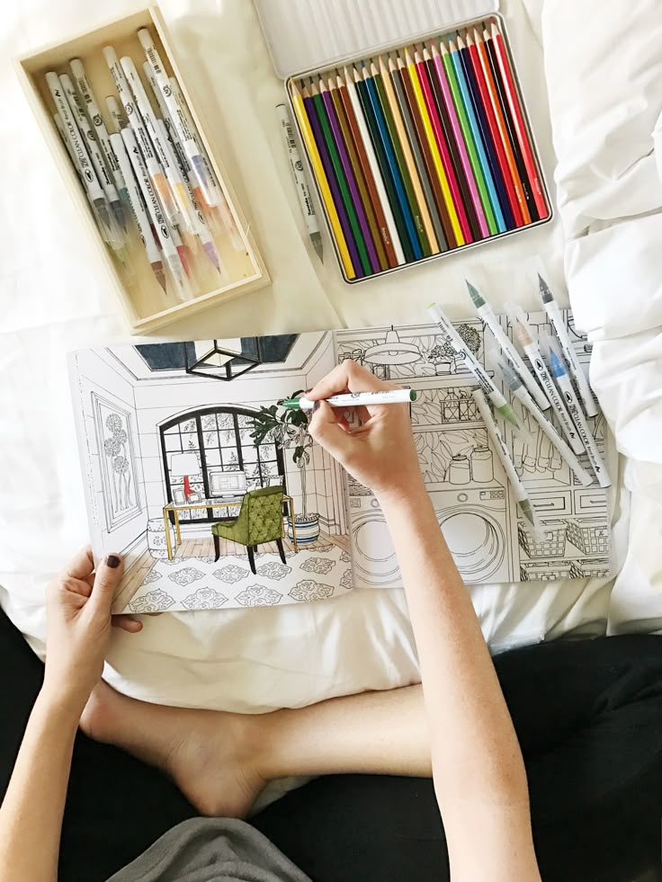 Person coloring intricate designs in a book with markers and colored pencils on a bed, creating relaxing art.