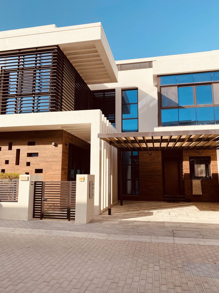 Modern house exterior with wooden accents, large windows, and pergola under a clear blue sky.
