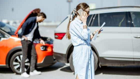 Common Mistakes in Motor Accident Claims Woman on phone at scene of minor car accident, man checking damaged vehicle. | Sky Rye Design Woman on phone at scene of minor car accident, man checking damaged vehicle.