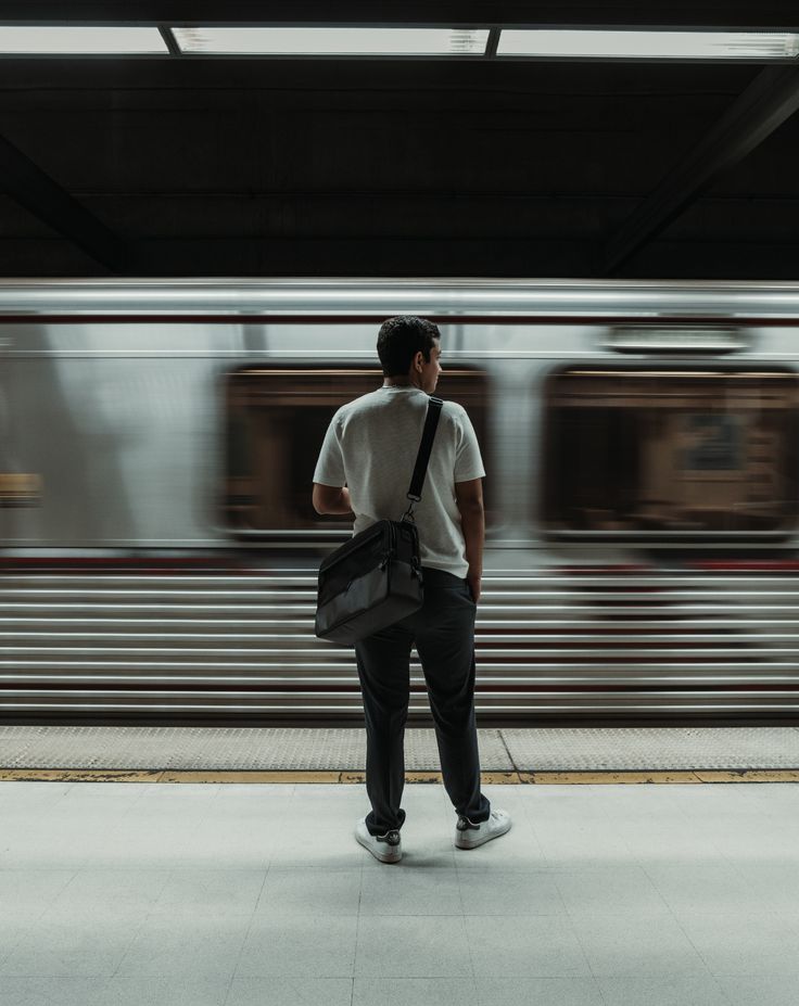 Man waiting for train on subway platform, with motion blur of passing train in the background.