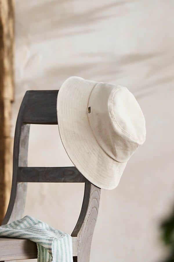 Cream sun hat on a wooden chair with striped fabric, creating a relaxed and stylish summer vibe.