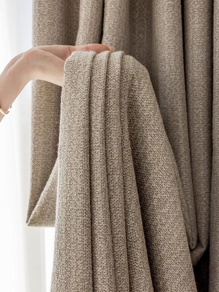 Hand holding textured beige curtain, showcasing fabric detail and folds.