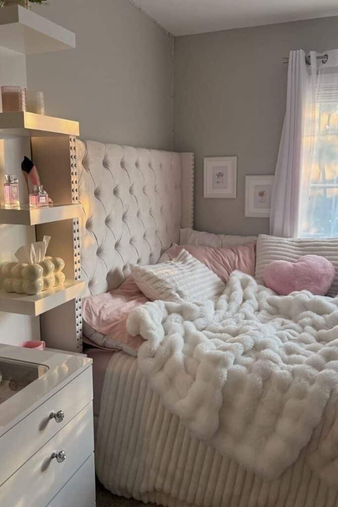 Cozy bedroom with pink and white decor, fluffy bedding, tufted headboard, and decorative shelves.
