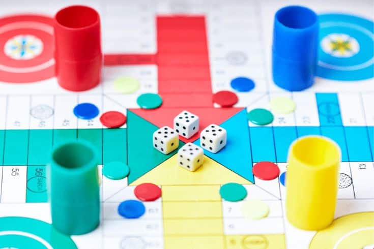 Colorful board game with red, yellow, and blue pieces, dice in the center, and a vibrant game board background.