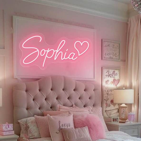 Chic pink bedroom with neon name sign above tufted headboard, featuring decorative cushions and wall art.