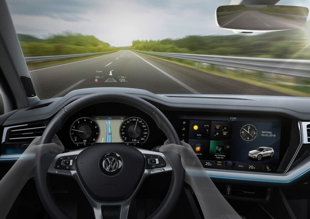 Driving view of modern car dashboard with navigation, digital displays, and steering wheel on a scenic highway.