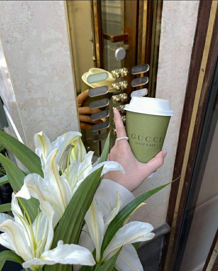 Person holds coffee cup and flowers, pressing doorbell at elegant entrance, showcasing Gucci lifestyle ambiance.