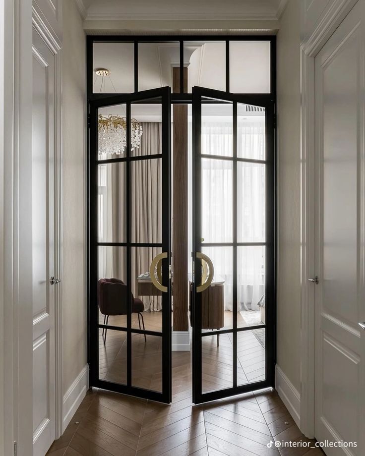 Elegant glass double doors with black frames open to a stylish room with a chandelier and soft curtains.