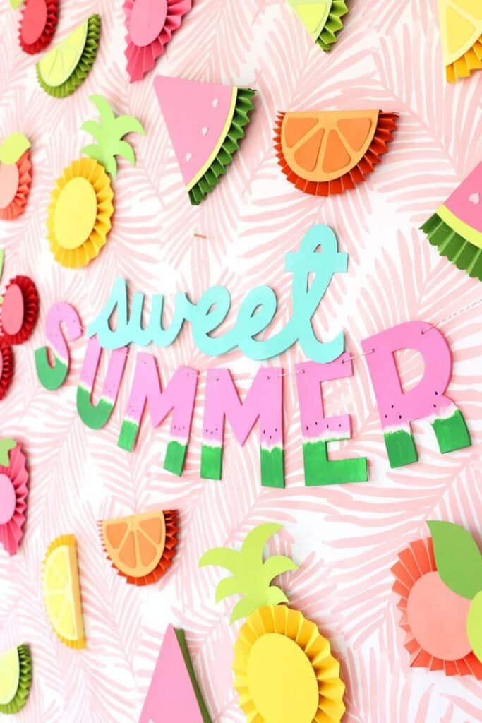Colorful Sweet Summer sign with paper fruit decorations on a pink patterned background. Bright, festive summer decor.