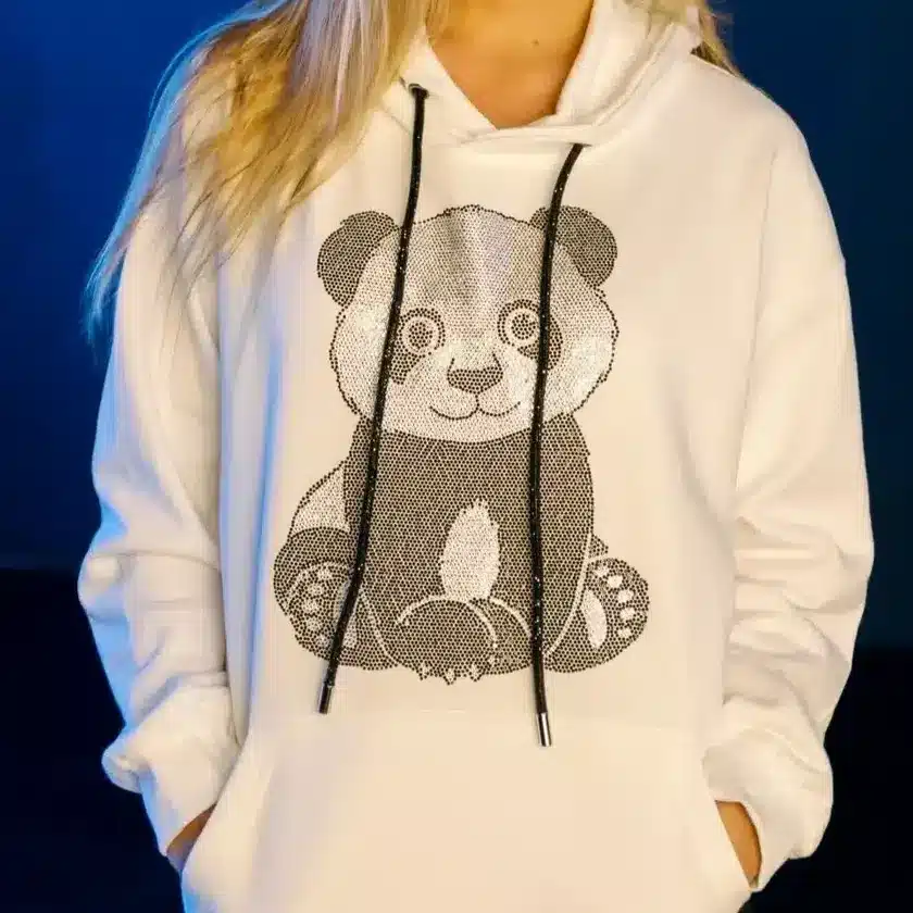 DSC_7575-1 Woman in a white hoodie with panda design, smiling against a blue background. | Sky Rye Design Woman in a white hoodie with panda design, smiling against a blue background.