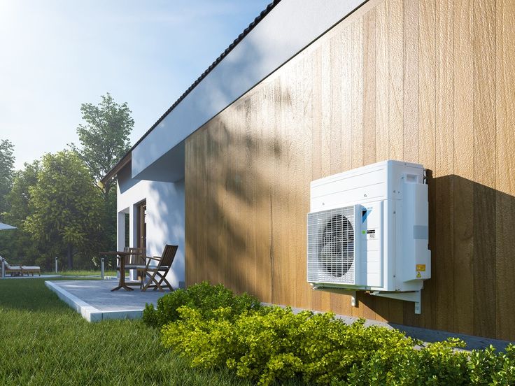 Exterior view of a modern house with a wall-mounted air conditioning unit and a patio surrounded by greenery.