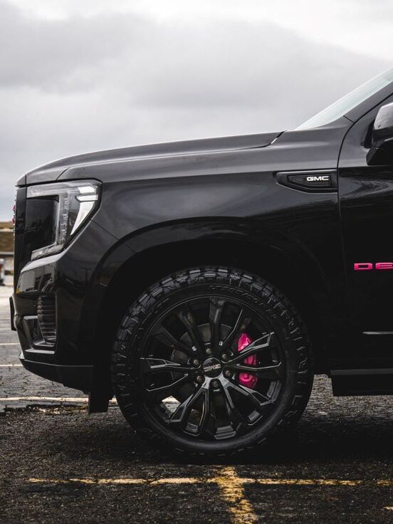 Close-up of a black GMC Denali SUV with stylish black wheels in a parking lot, under overcast sky.