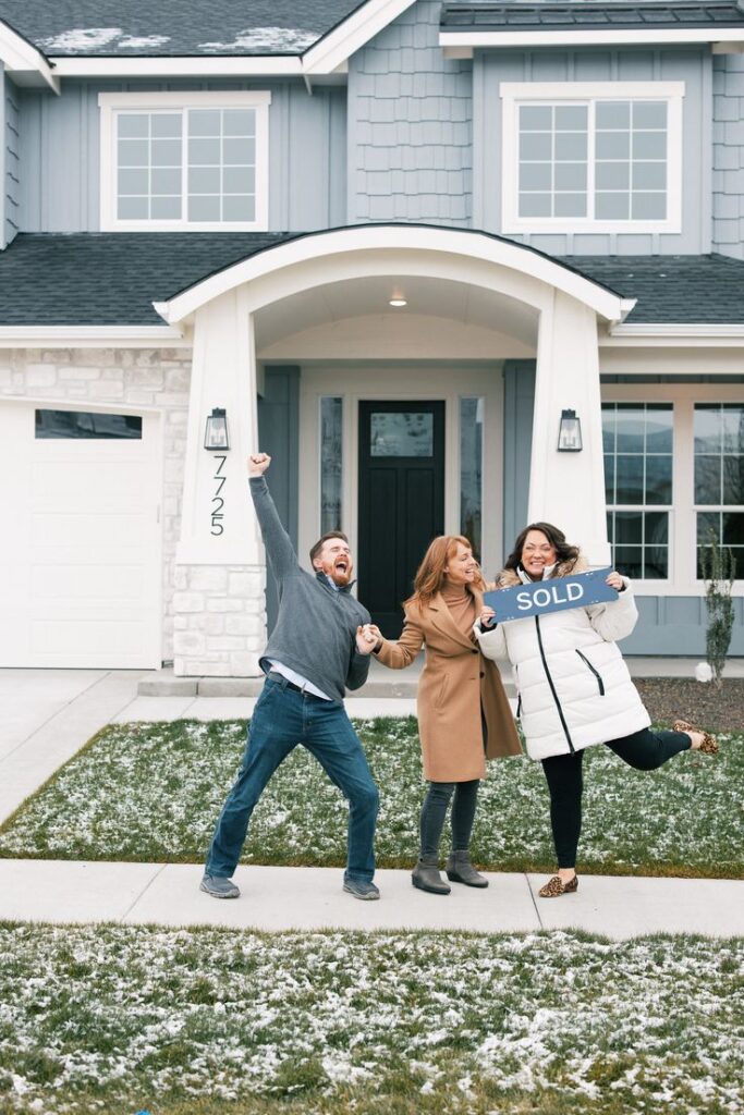 Group celebrating in front of new home holding SOLD sign on snowy lawn.