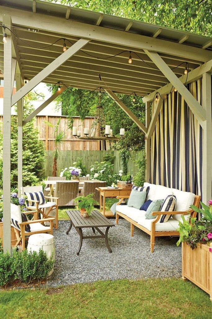 Outdoor lounge under pergola with seating, table, chandelier, and vibrant plants for a cozy garden retreat.