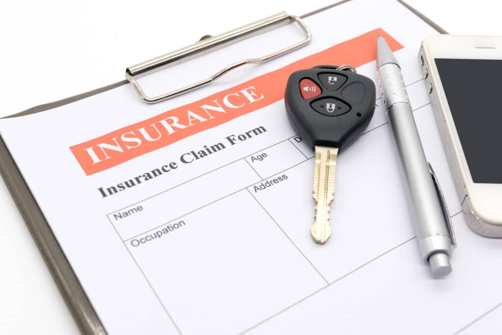 Car insurance claim form with car key, pen, and smartphone on clipboard.