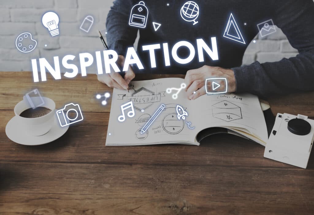 Person drawing creative ideas in notebook with digital icons representing inspiration and creativity around.