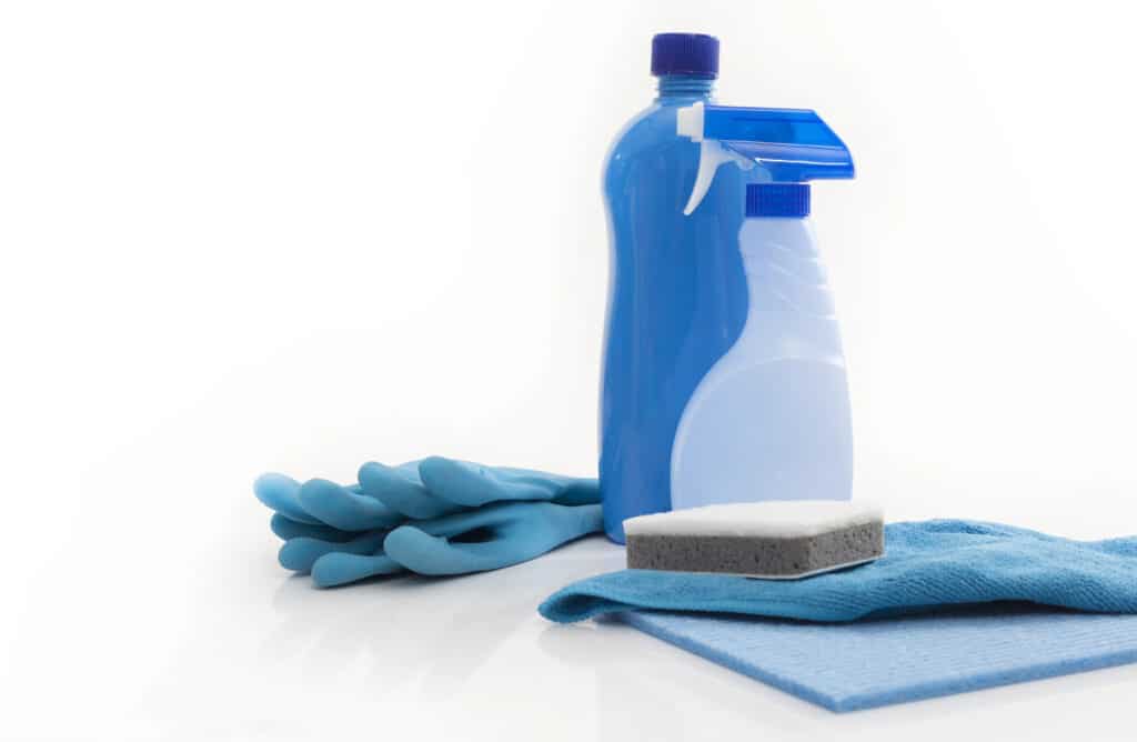 Cleaning supplies including blue gloves, spray bottle, sponge, and cloth on white background.