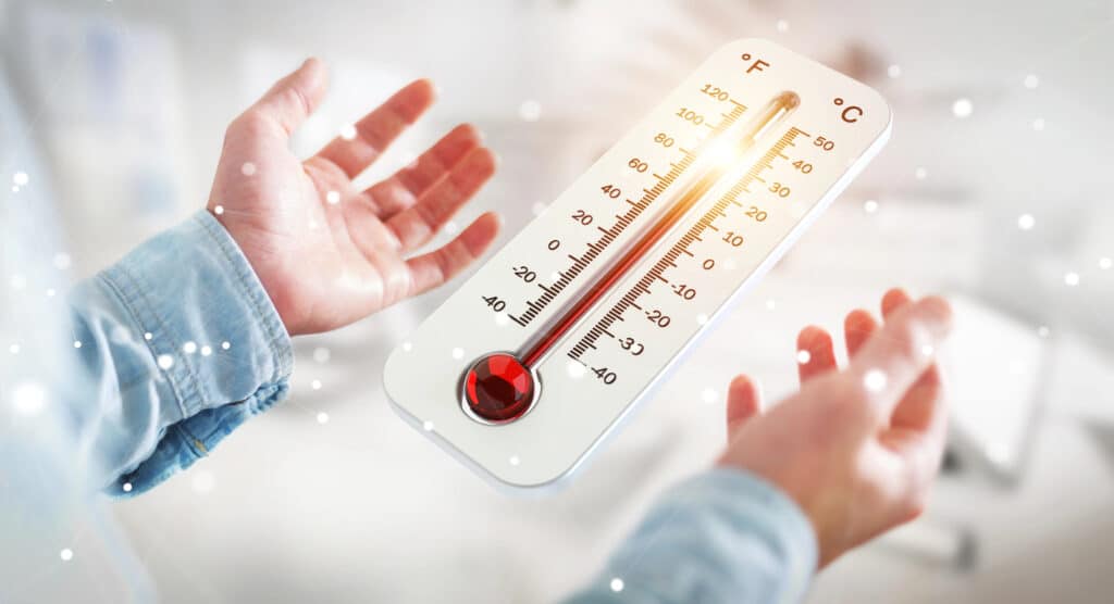 Hands holding a glowing thermometer showing temperature in Fahrenheit and Celsius.