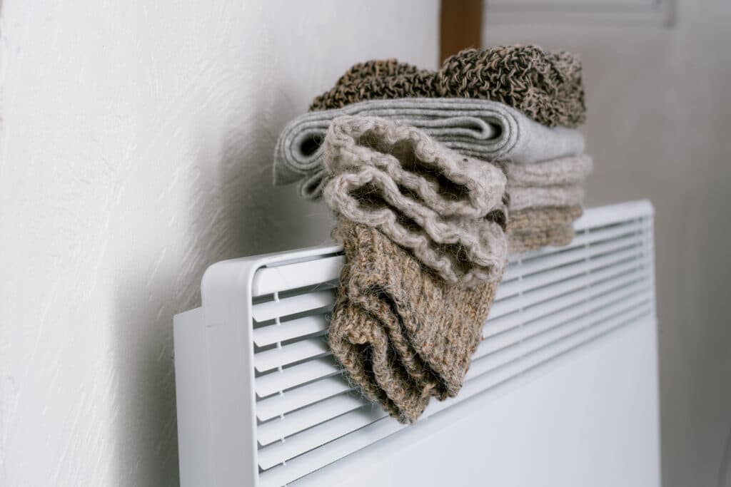 Woolen clothes drying on a white heater in a cozy indoor setting.