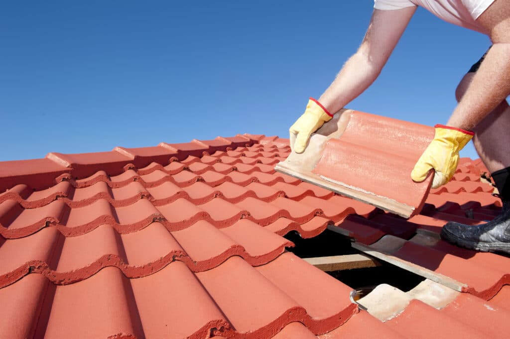 Depositphotos_19661037_XL Person replacing red roof tiles against clear blue sky. Roof repair maintenance. | Sky Rye Design Person replacing red roof tiles against clear blue sky. Roof repair maintenance.