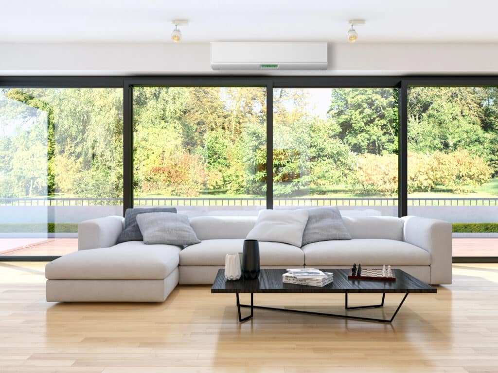 Depositphotos_201949970_XL Modern living room with large windows, featuring a gray sectional sofa and sleek coffee table overlooking a lush garden view. | Sky Rye Design Modern living room with large windows, featuring a gray sectional sofa and sleek coffee table overlooking a lush garden view.