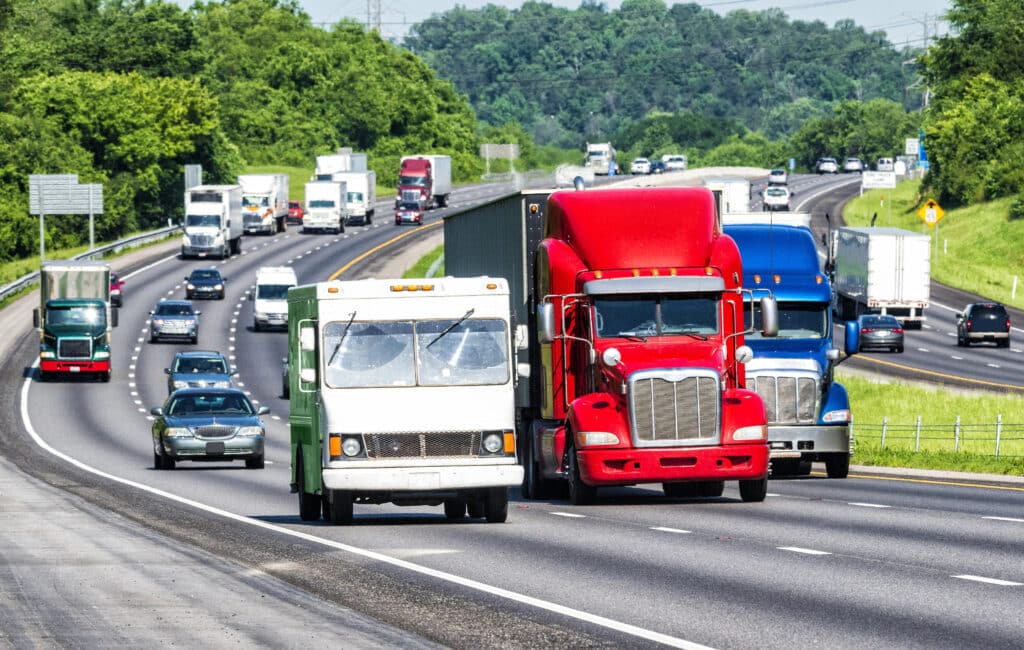 Trucks and cars driving on a busy highway surrounded by greenery on a clear day.