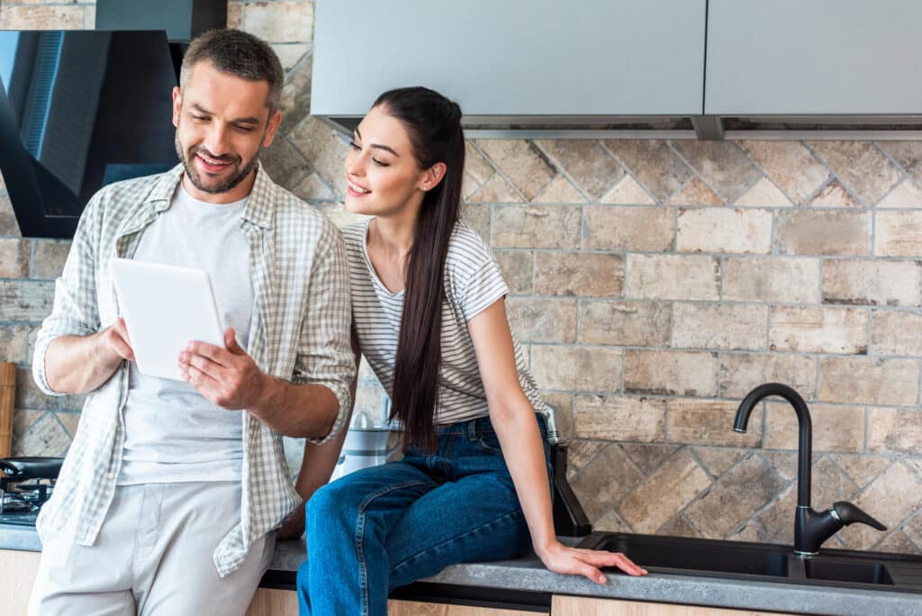 Couple in modern kitchen using a tablet together, smiling and engaging with technology.