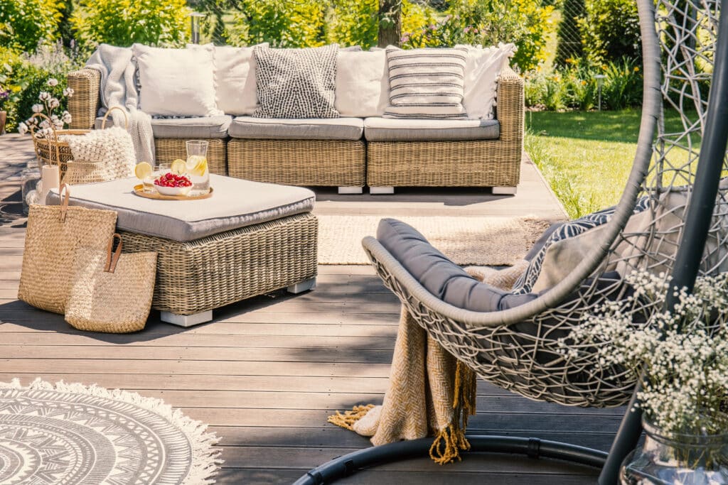 Cozy outdoor patio with wicker furniture, decorative pillows, and a hanging chair, perfect for relaxation and gatherings.