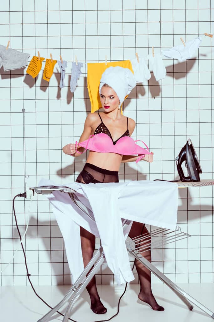Woman ironing in lingerie with clothesline, stylish laundry room setting.