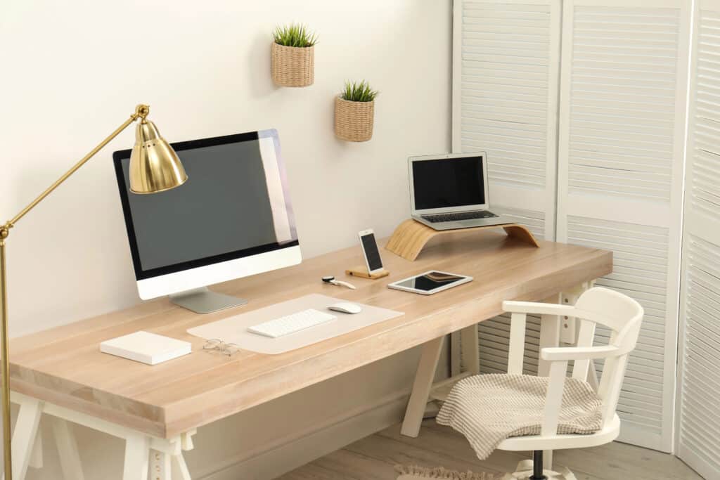 Modern workspace with desktop, laptop, and smartphone on a wooden desk, accented by a gold lamp and minimal decor.
