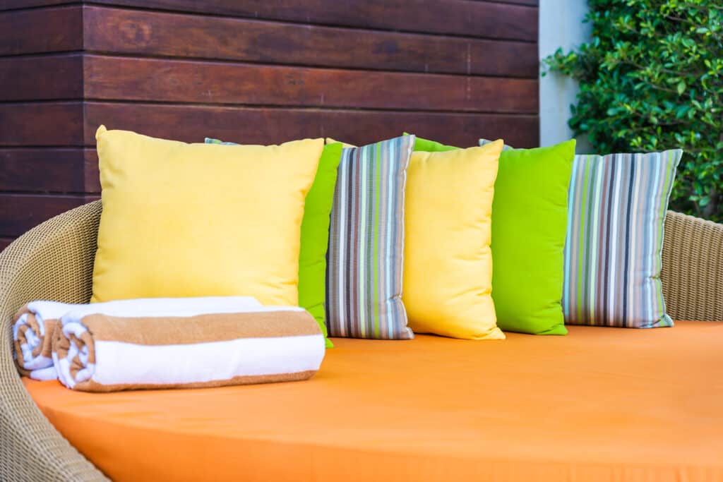 Colorful patio cushions and rolled towels on an orange lounge chair, perfect for outdoor relaxation.